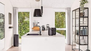 A modern kitchen with a central island, a coffee machine, and a glass cabinet with dishes. - 12 Person Holiday Home in Vaeggerlose (Vaeggerlose)