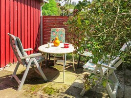 Un patio con una mesa redonda, dos sillas, un muro rojo y un jardín.