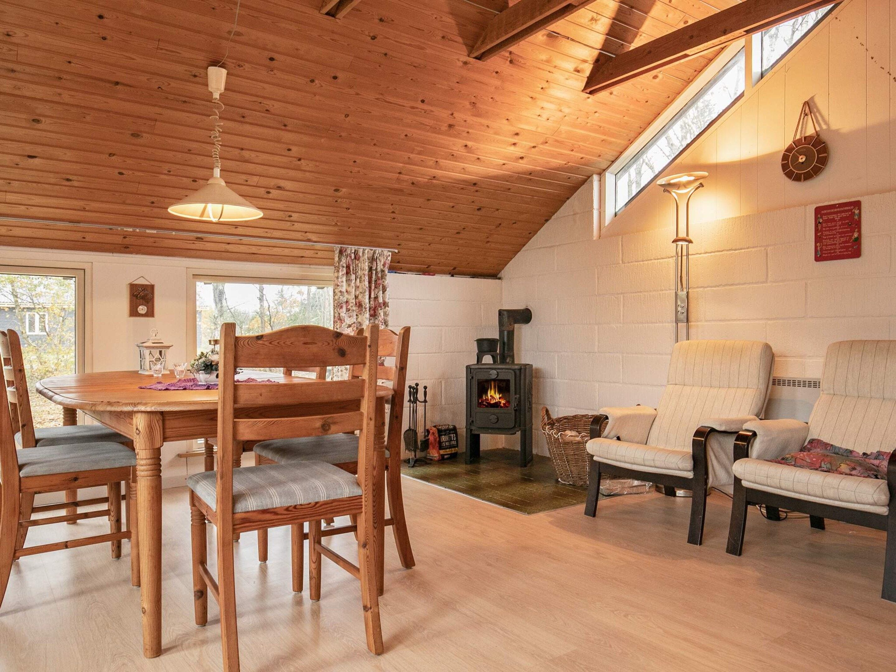 Ein gemütliches Blockhaus-Interieur mit Esstisch, Stühlen, einer Couch und einem Kaminofen.