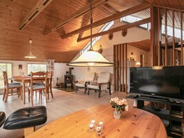 A cozy living room with a wooden ceiling, a fireplace, a dining area with chairs, a sofa, a TV, and a wooden table with a vase and candles.