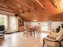 Una habitación acogedora con techo de madera, una mesa de comedor con sillas, un sofá, una chimenea y una ventana con cortinas.