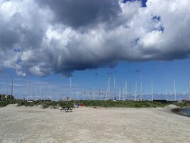 A sandy beach with wind turbines in the background and flags on poles.