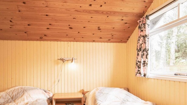 Une chambre avec deux lits, une table de chevet avec des tiroirs, une lampe et une fenêtre ornée de rideaux à motifs floraux.