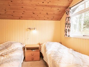 A room with two beds, a nightstand with drawers, a lamp, and a window with floral curtains. - 4 Person Holiday Home in Hals (Hals)