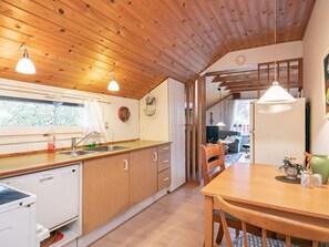 A kitchen with wooden cabinets, a dishwasher, and a dining area with a table and chairs. - 4 Person Holiday Home in Hals (Hals)