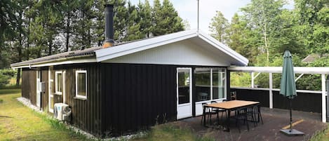 A small, single-story building with a covered patio area, a table and chairs, and a chimney.