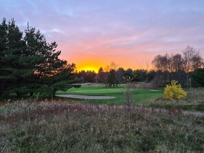 A golf course at sunset with a pond, trees, and a clear sky.