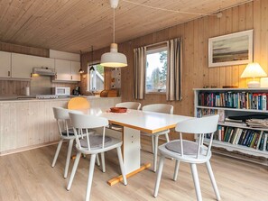 A modern kitchen with wooden cabinets, a white countertop, and a dining area with a white table and chairs. - 6 Person Holiday Home in Fjerritslev (Fjerritslev)