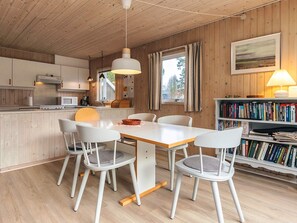 A modern kitchen with white cabinets and a wooden ceiling, a dining area with a white table and chairs, and a bookshelf filled with books. - 6 Person Holiday Home in Fjerritslev (Fjerritslev)