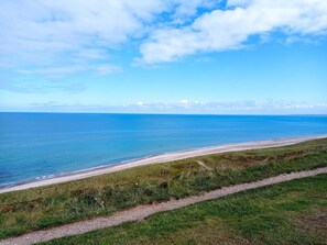 A coastal landscape with a clear sky, a sandy beach, and a grassy path leading to the shore. - 6 Person Holiday Home in Fjerritslev (Fjerritslev)