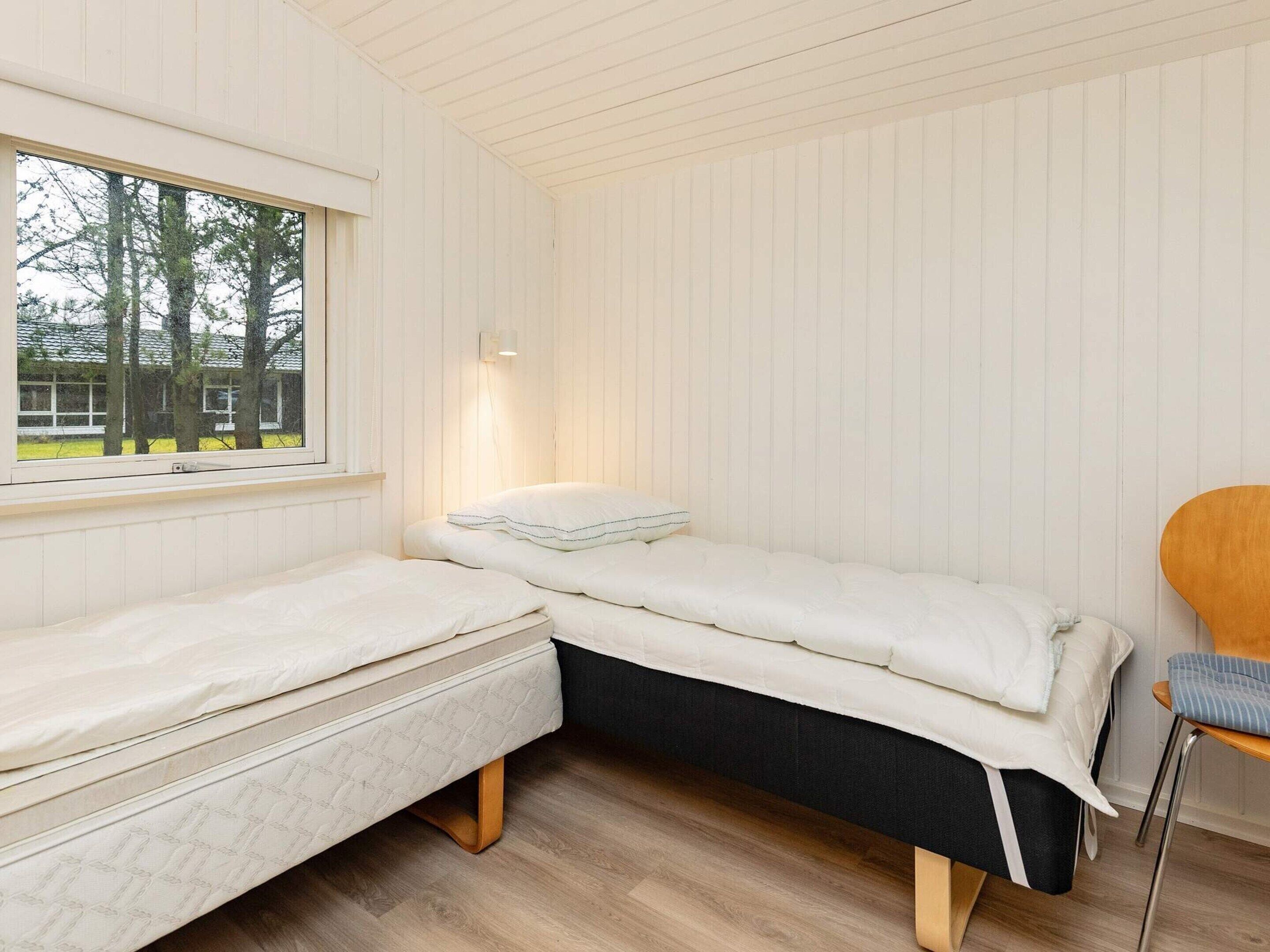 A room with a bed, a chair, and a window with a view of trees.