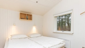 Un dormitorio con una cama, dos lámparas de pared, un ventanal con vistas a árboles y un estante de madera sobre la cama.