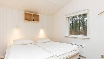 A bedroom with a bed, two wall-mounted lights, a window with a view of trees, and a wooden shelf above the bed.