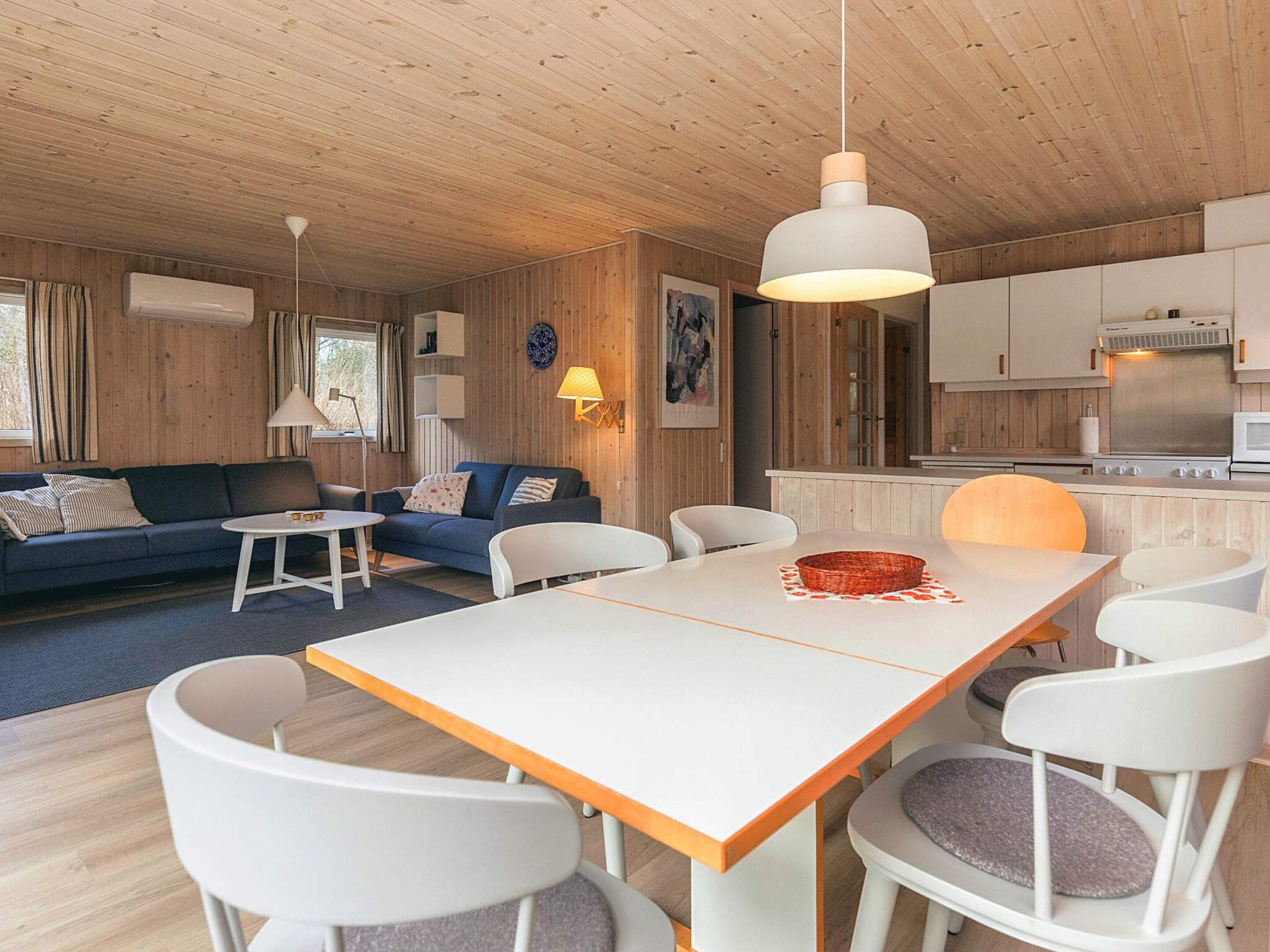 A modern interior with a dining area, sofa, kitchen, and a hanging light fixture.