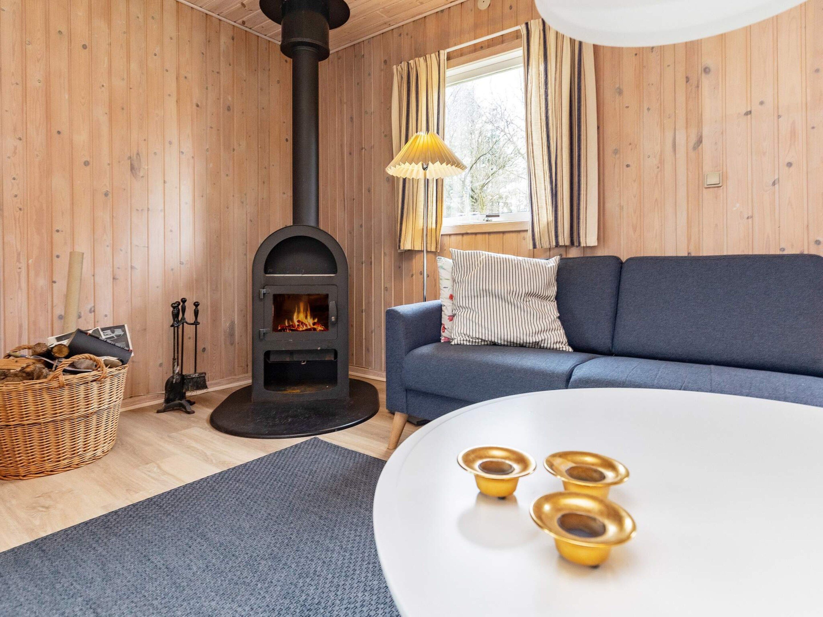 Une pièce chaleureuse avec une cheminée, un canapé, une table blanche et un panier de bois de chauffage.