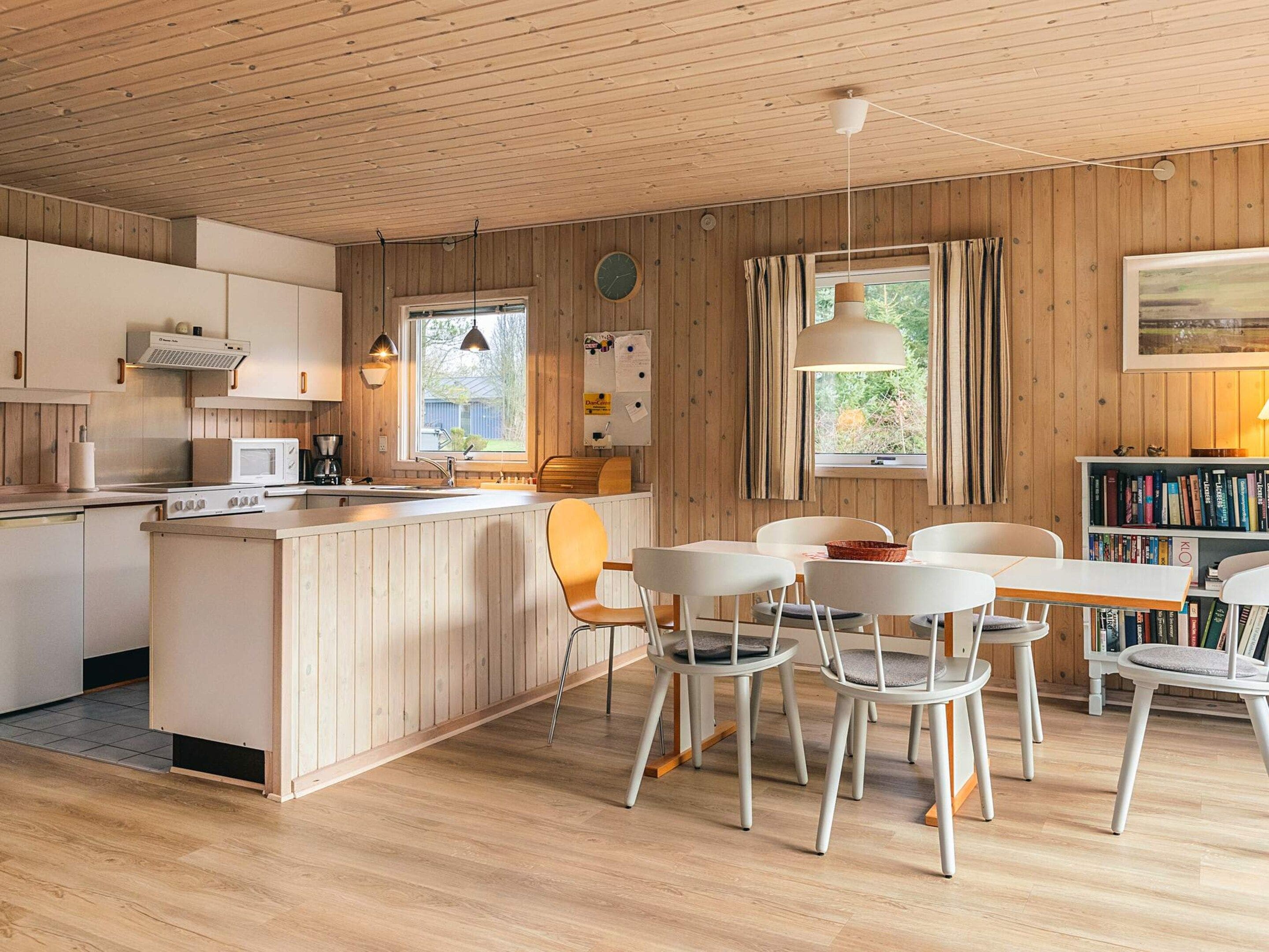 A modern kitchen with wooden cabinets, a central island, and white chairs around a table.