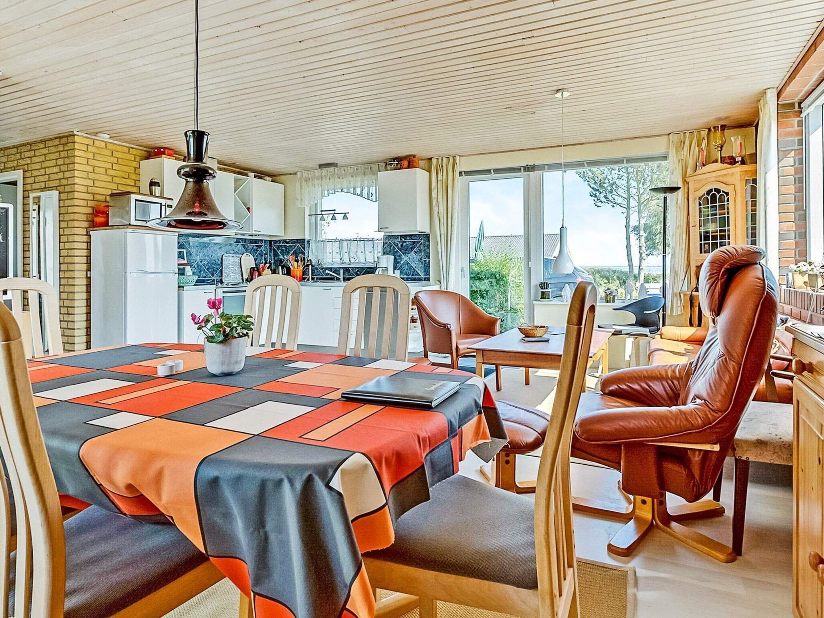 Ein Essbereich mit einem Tisch, gedeckt für vier Personen, umgeben von Stühlen, mit Blick auf die Küche und den Garten durch große Fenster.