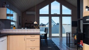 Eine moderne Küche mit Holzausstattung, ein Essbereich mit Tisch und Stühlen sowie eine große Schiebeglastür, die auf eine Terrasse führt.
