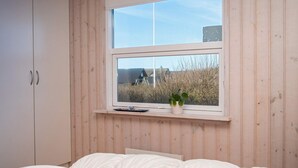Ein Schlafzimmer mit einem Bett, einem Fenster mit Blick auf ein Haus und Büsche sowie einem Holzschrank.