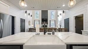 A modern kitchen with white cabinetry, a large marble island, and pendant lighting. - Family Fun! Private suites, garden games, fire pit & kids loft!  (Broken Bow)