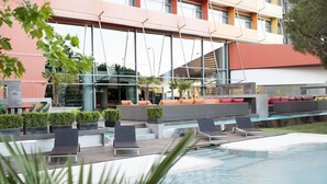 A modern outdoor pool area with lounge chairs and seating, surrounded by a building with large windows and a geometric facade. - Puerta America Madrid (Madrid)