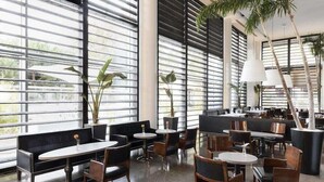 A modern cafe with black and white furniture, large windows, and indoor plants. - Puerta America Madrid (Madrid)