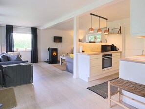 A modern living room with a sofa, a fireplace, and a kitchen area with a microwave and oven. - 4 Person Holiday Home in Gilleleje (Gilleleje)