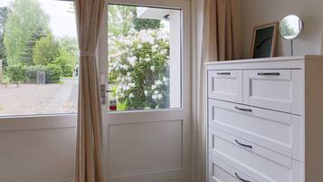 A room with a white door, beige curtains, a white cabinet with drawers, and a small round mirror on the wall.