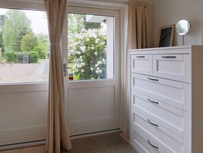 A room with a white door, beige curtains, a white cabinet with drawers, and a small round mirror on the wall. - 4 Person Holiday Home in Gilleleje (Gilleleje)