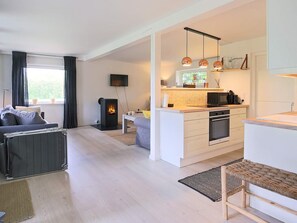 A modern living room with a sofa, a fireplace, and a kitchen area with a microwave and oven. - 4 Person Holiday Home in Gilleleje (Gilleleje)