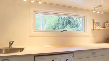 A kitchen with a built-in washing machine, a window with a view of trees, and a shelf with items.
