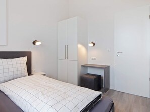 Ein Schlafzimmer mit Bett, Kleiderschrank, Nachttischen und Wandleuchten.