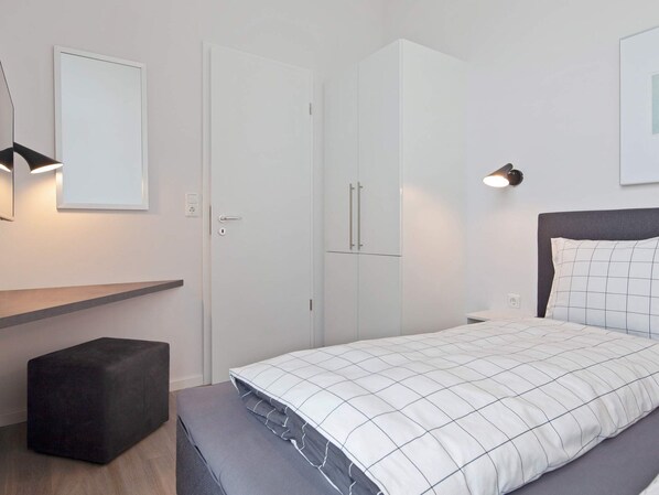 A bedroom with a bed, a wardrobe, a bench, and a wall-mounted light fixture.