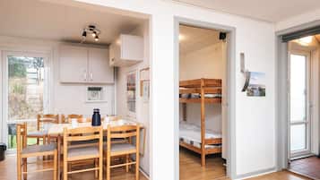 Ein kleines Zimmer mit Etagenbett, Esstisch und Stühlen sowie einer Küchenzeile mit Schränken.
