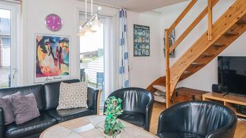 Una sala de estar con un sofá de cuero negro, una mesa de centro con una planta, un televisor y una escalera de madera.