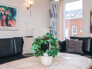 A modern living room with a black leather sofa, a round coffee table with a decorative plant, a framed painting on the wall, and a window with curtains.