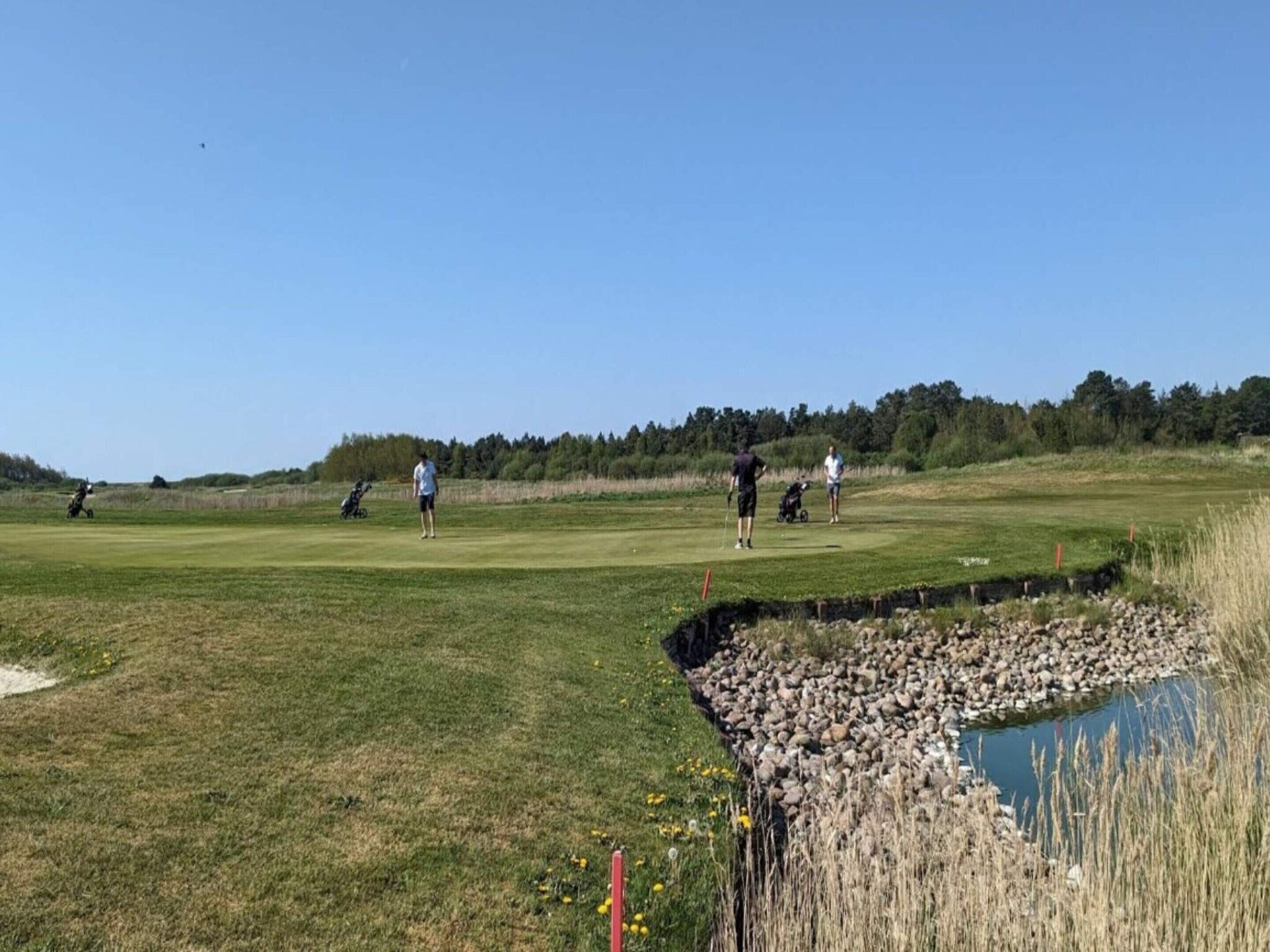 Un campo de golf con un estanque, árboles y cielo despejado.