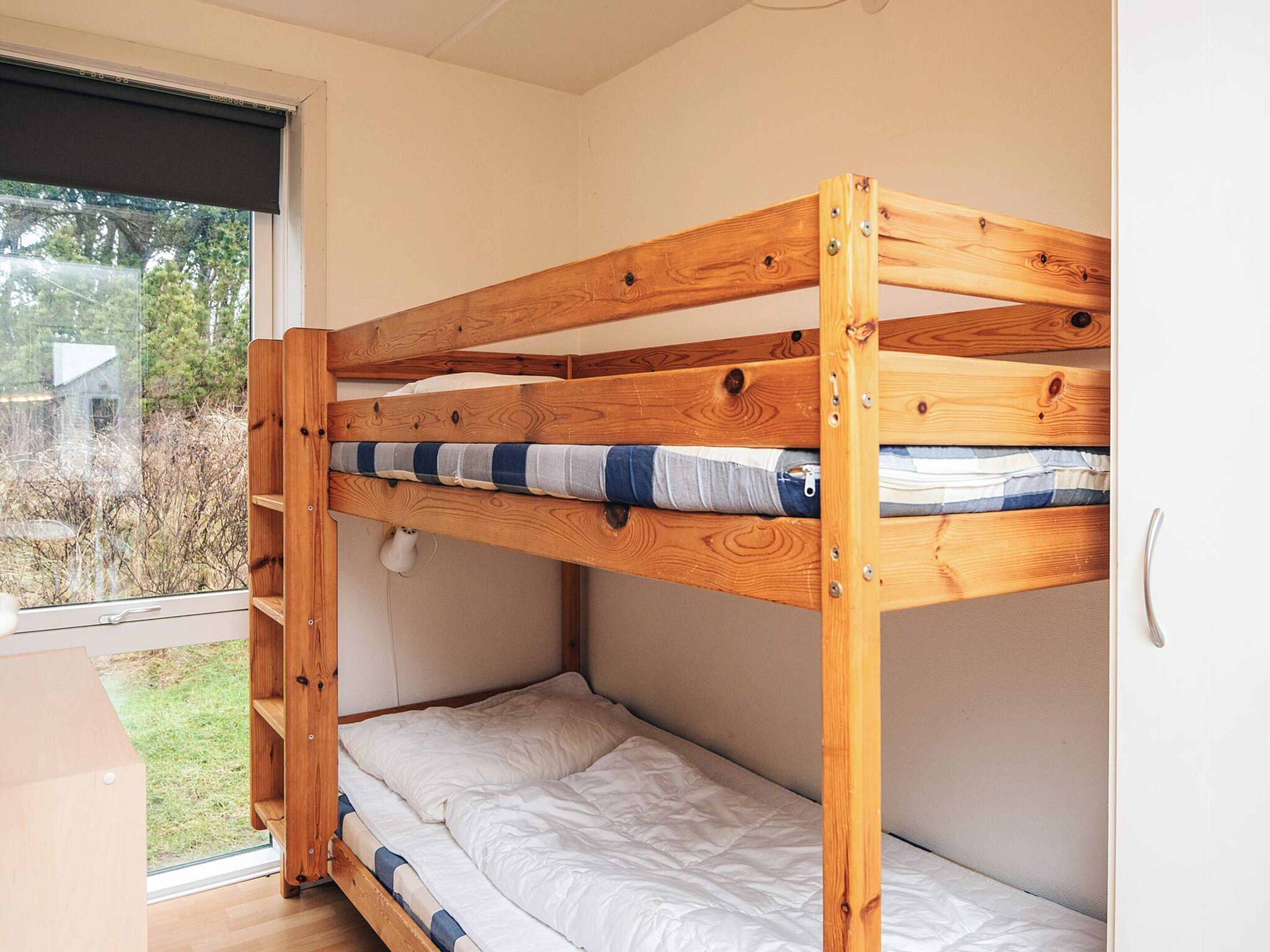 Un lit superposé avec une structure en bois, une fenêtre donnant sur un paysage verdoyant et une porte blanche.