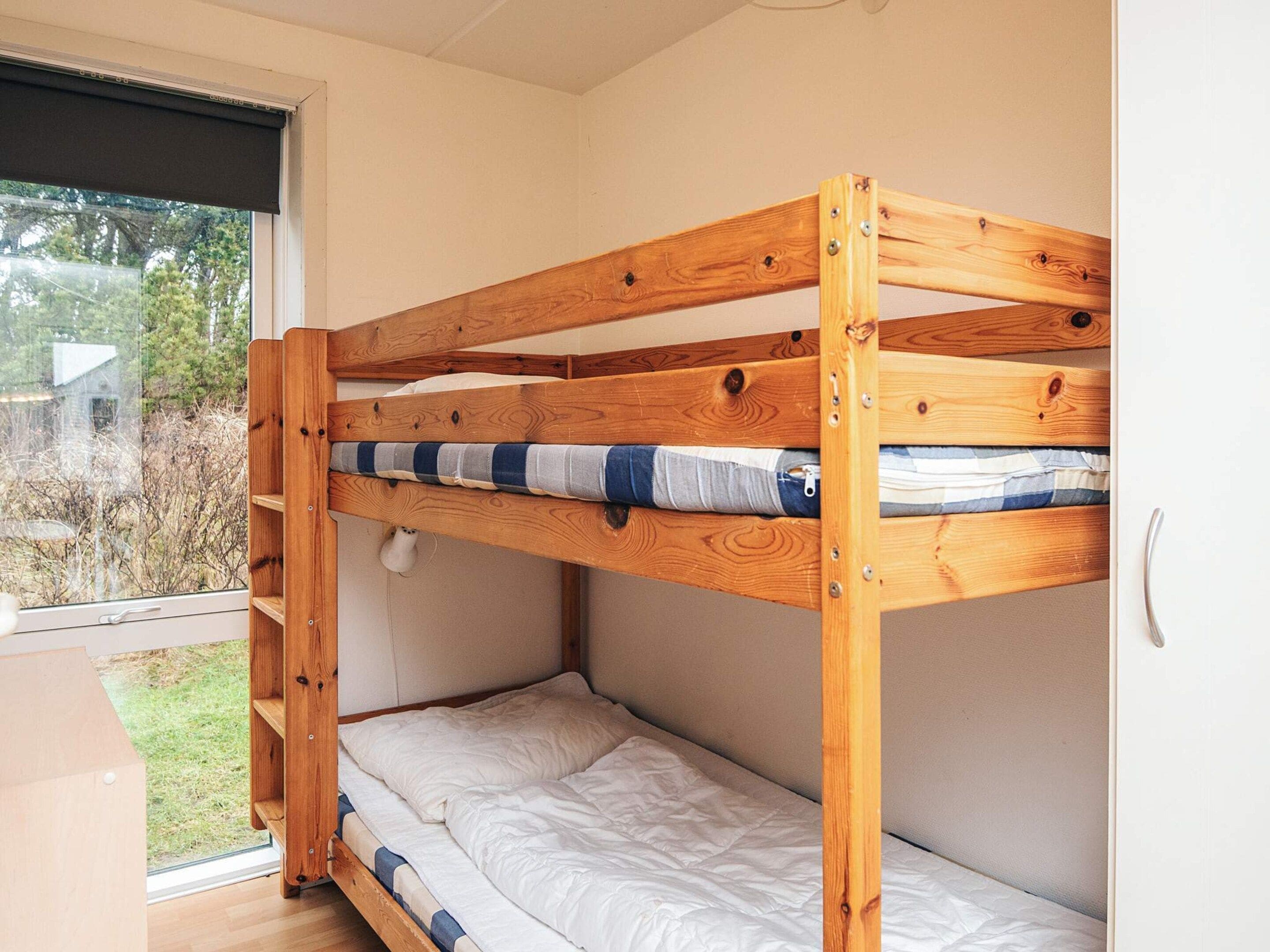 A bunk bed with a wooden frame and a window with a view of the outdoors.
