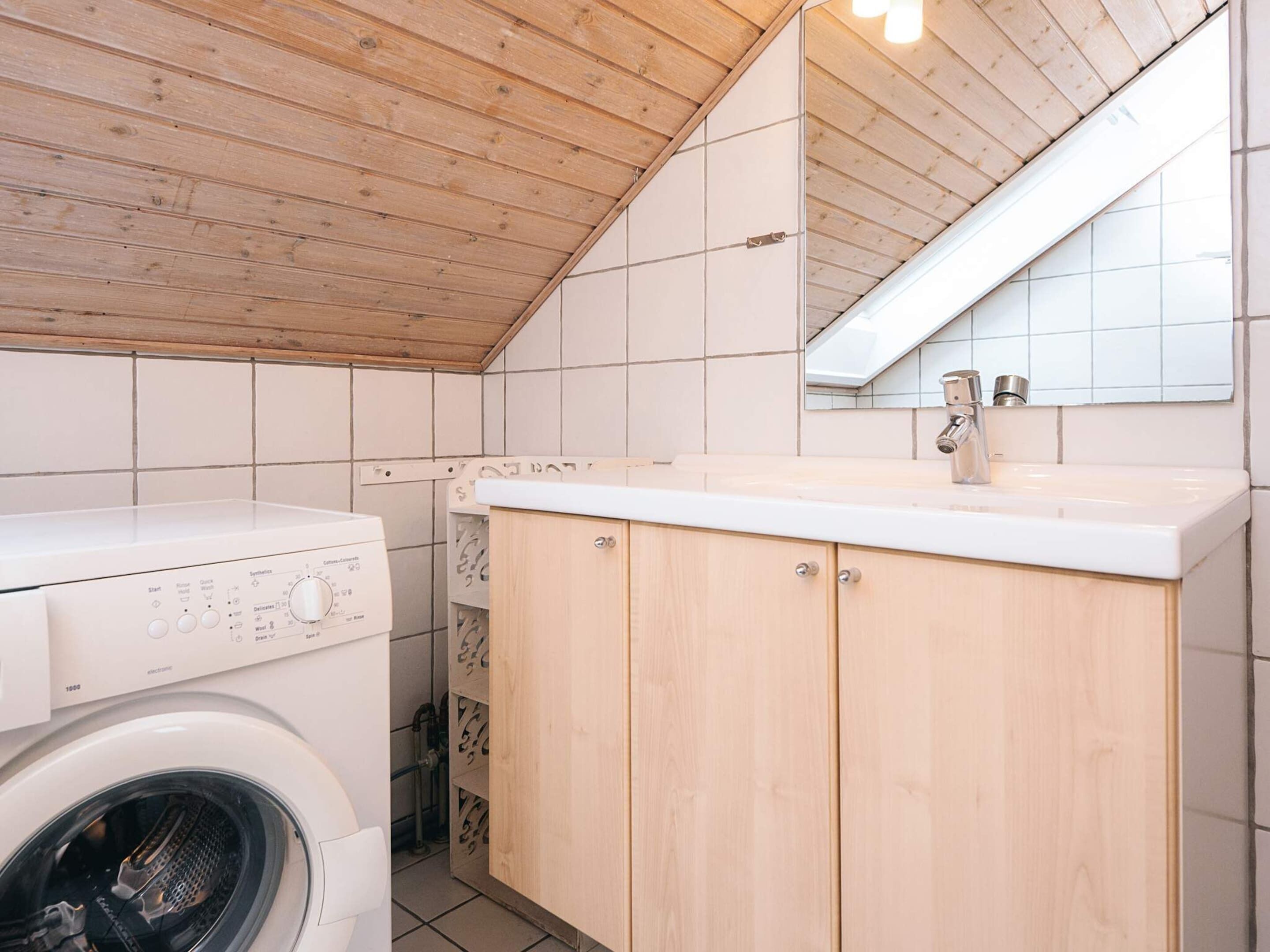 Une buanderie équipée d’un lave-linge à chargement frontal, de meubles en bois et d’un mur recouvert de carreaux.