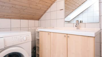 Ein Waschraum mit einer Waschmaschine mit Frontlader, Holzschränken und einer gefliesten Wand.
