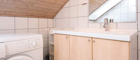 Une buanderie équipée d’un lave-linge à chargement frontal, de meubles en bois et d’un mur recouvert de carreaux.
