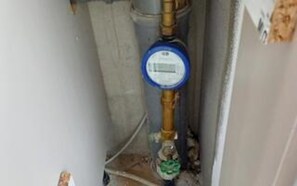 Contador de agua con pantalla digital, una llave de bronce y una llave verde, probablemente parte de una instalación de fontanería.