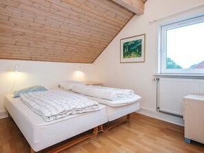 A bedroom with a sloped ceiling, two beds, a radiator, a window, and a painting on the wall. - 6 Person Holiday Home in Romo (Rømø)