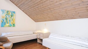 Um quarto aconchegante com teto inclinado, piso de madeira, duas camas com roupa de cama branca, uma cadeira e um quadro na parede.