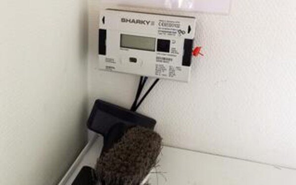 Un termostato fijado a la pared con pantalla digital, un botón rojo de emergencia y un dispositivo negro debajo.