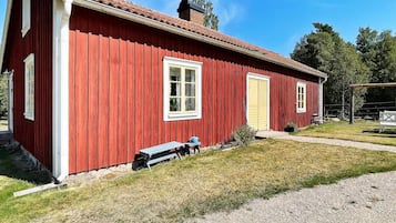 A red wooden building with a tiled roof, a bench, and a small garden area.