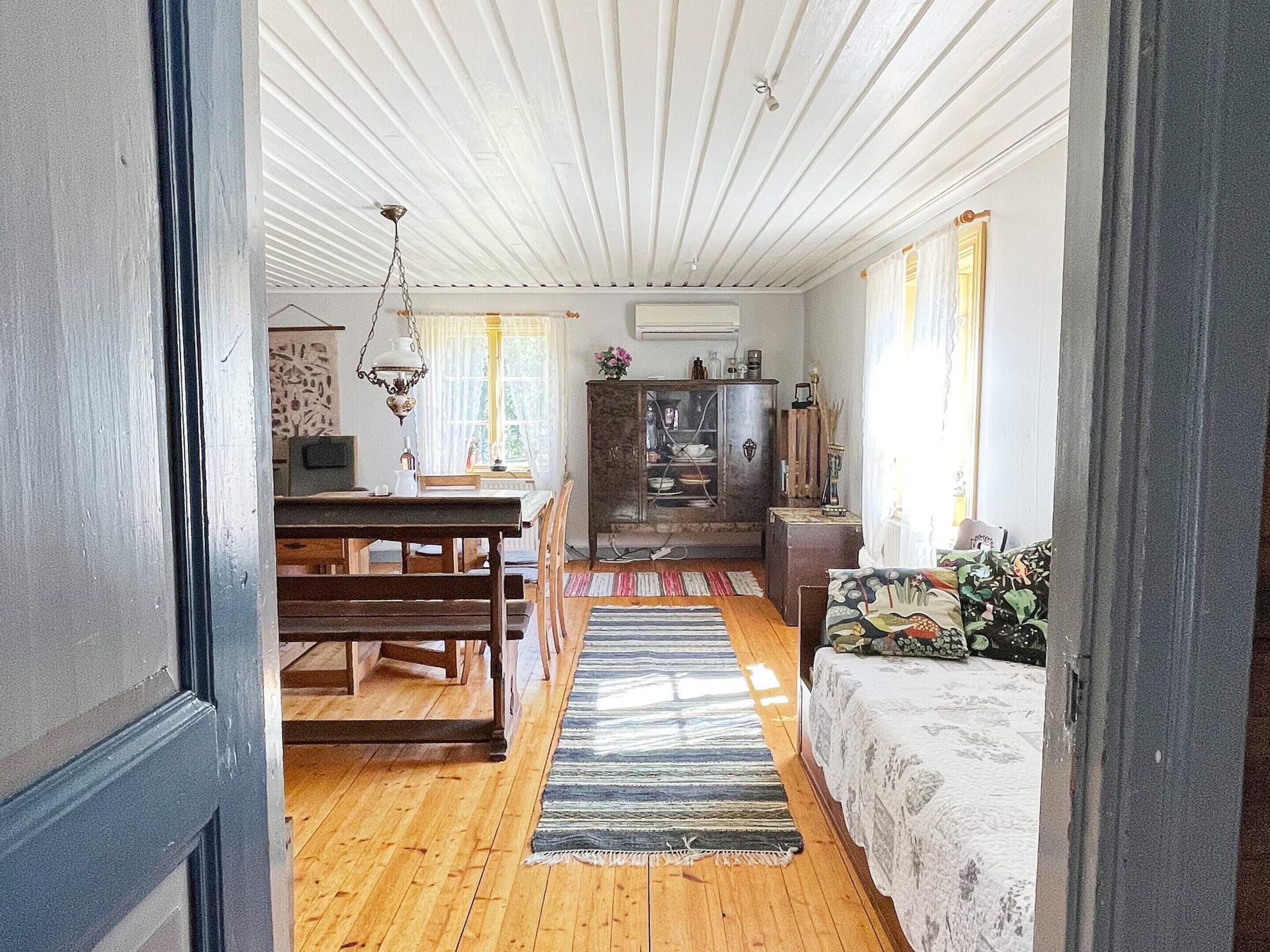 A room with a wooden floor, a dining table with chairs, a sofa, a cabinet, and a hanging light fixture.