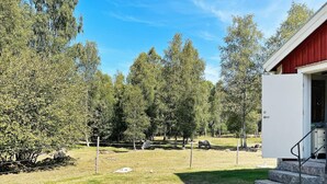 A fenced outdoor area with a building entrance, trees, and a grassy field. - 4 Person Holiday Home in Furuby (Hovmantorp)