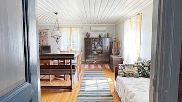 A room with a wooden floor, a dining table with chairs, a sofa, a patterned rug, and a cabinet with glass doors.